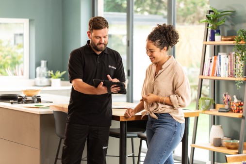 Un installateur elm.leblanc conseille une cliente avec une tablette dans une cuisine.